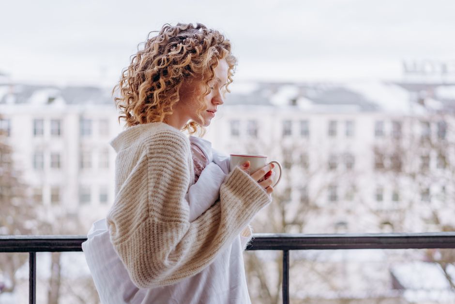 A person standing outdoors in soft morning light, holding a warm mug