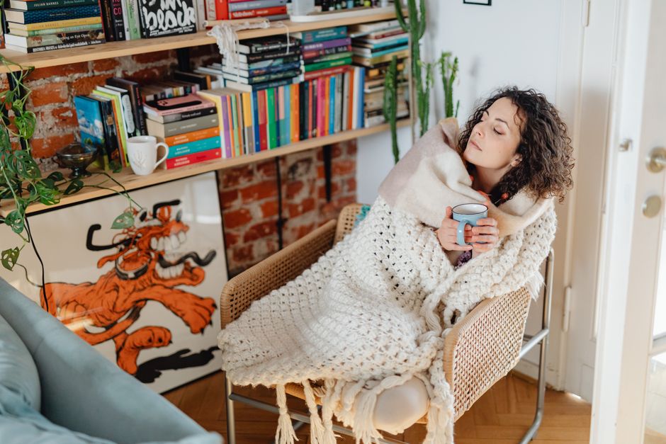 A warm mug and folded blanket resting on a chair by a window