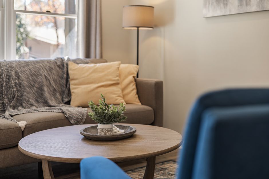 A softly lit living room corner with a lamp, a warm drink, and a folded blanket at dusk